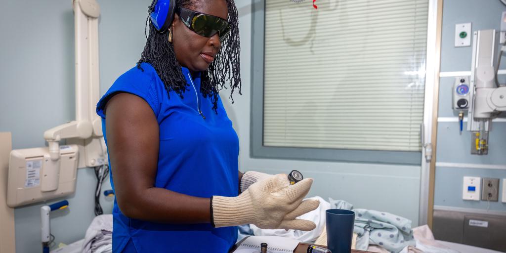 Woman in blue scrubs and safety glasses working in a hospital room.