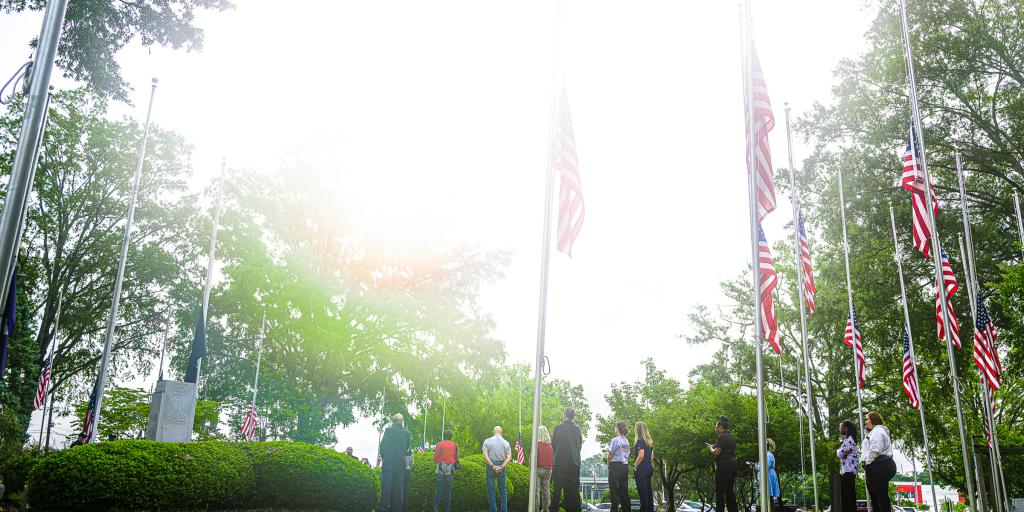 Group of people standing at attention in front of flagpoles.