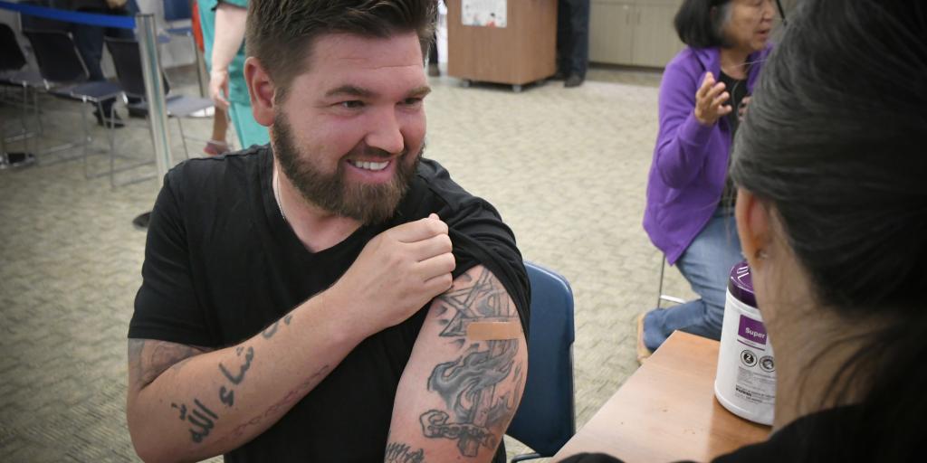 Man with tattoos gets a vaccine from a nurse.