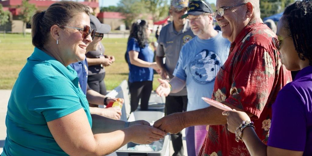 A group of people standing outdoors, shaking hands and smiling.