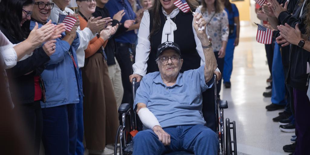 Elderly man in wheelchair applauded by hospital staff.