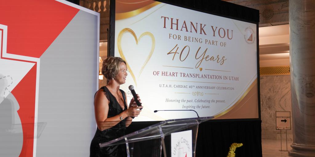 Woman standing at podium with microphone, addressing audience. Large screen behind her reads "Thank you for being part of 40 years".