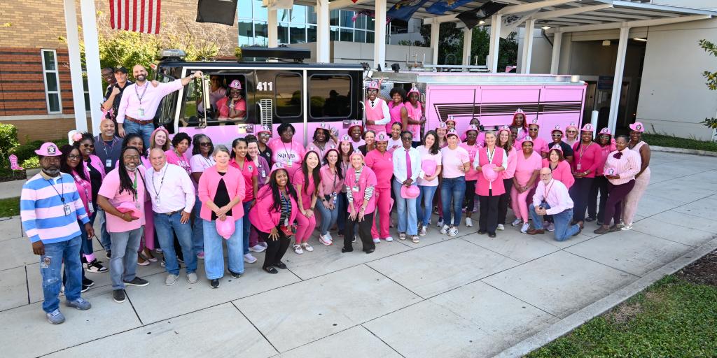 Group of people in pink clothing standing in front of a pink bus.