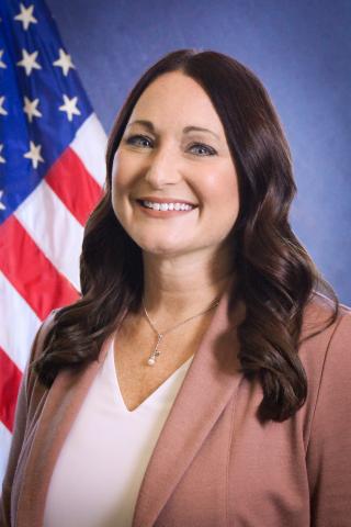 Headshot of Carrie Hensley in front of U.S. flag with a blue background.