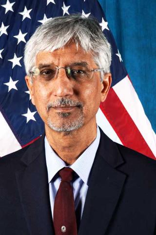 Dr. Zahoor A. Waseem is wearing a blue suit and maroon tie standing in front of the American Flag.