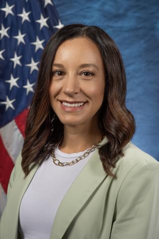 Portrait of a woman with brown hair and tan skin wearing a light green blazer over a white shirt.