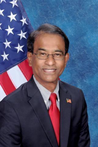 Dr. javed Tunio poses in front of blue background with an American flag over his right shoulder.