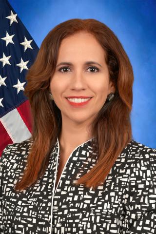 Ana Almodovar with a blue background and the American Flag to her left side. 