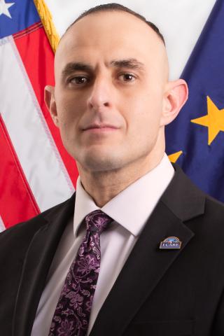 Executive Director Thomas Talamante posing for headshot in front of American and VA Executive flag.