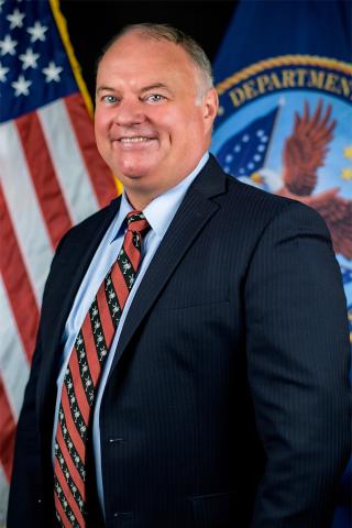 Jeffrey Soots poses for a photo with the U.S. and VA flags in the background. 
