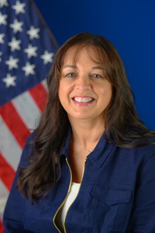 Ms. Sinay poses for a photo in front of the U.S. flag and a blue background.