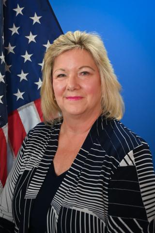 A woman with blonde hair posing for a portrait in front of an American flag and blue backdrop.