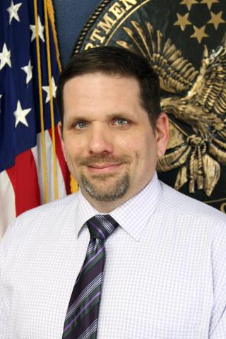 headshot of man in shirt and tie with American flag