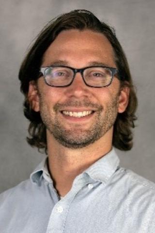 Headshot of a man with dark hair, eye glasses, button-up shirt.