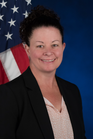 Kimberly with a dark blue background and flag background sitting tall and smiling