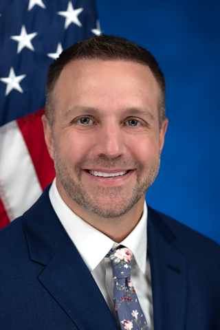 Portrait of a Dr. Derek Szafranski sitting with an American flag over his left shoulder. 