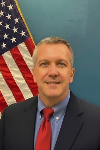 Caucasian man in a suit and tie in front  of American Flag