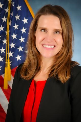 Portrait of a woman in red and black, smiling in front of an American flag.