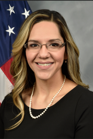 Woman in black shirt and pearl necklace smiling in front of US flag.