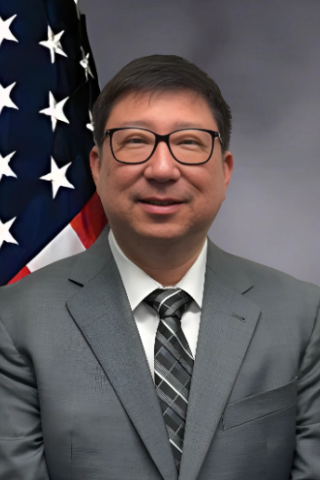 Man in suit and tie smiling with American flag behind him.