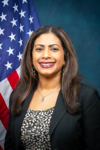 Woman with long hair smiling in front of American flag.