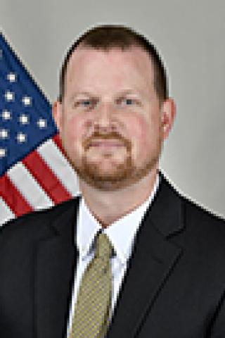 Man in a suit and tie standing in front of an American flag.