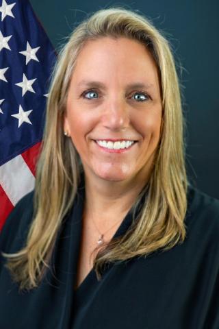 Woman with blonde hair smiling with an American flag behind her.