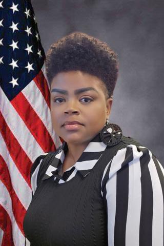 Woman in black and white striped shirt with American flag behind her.