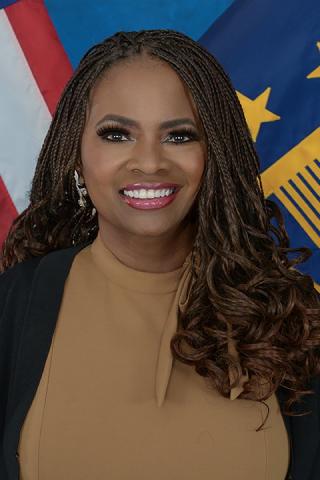 Woman with braided hair, smiling, in front of American and European Union flags.