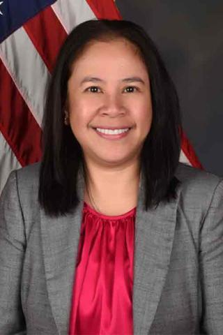 Portrait of a woman in business attire smiling with an American flag in the background.