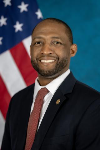Portrait of a man in suit and tie standing in front of an American flag.