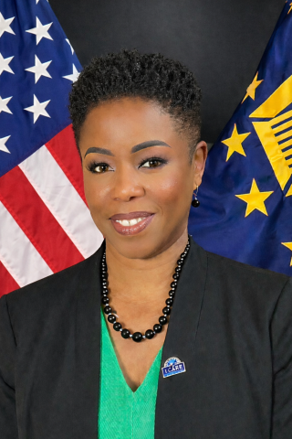 Woman in black blazer and green shirt with American behind her.