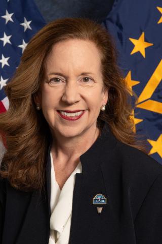 Portrait of a smiling woman with the American flag and a blue flag behind her.