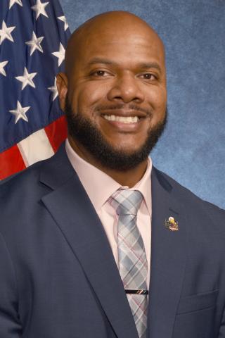 Smiling man in suit and tie with American flag in background.