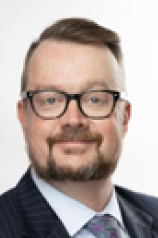 Man with short hair, beard, glasses, and a smile wearing a suit and tie.