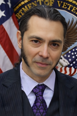 Man in a suit with a US flag and Department of Veterans Affairs logo in the background.