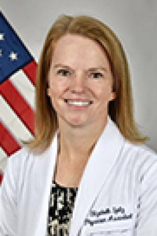 Woman in white lab coat with an American flag in the background.