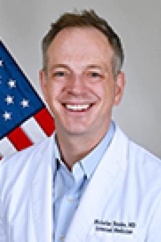 A smiling doctor in white coat with American flag in the background.
