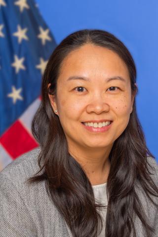 Woman with long black hair smiling in front of an American flag.