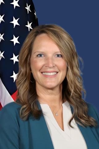 Woman smiling with American flag behind her, on blue background.
