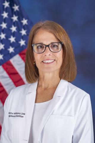 A woman in a white lab coat smiles in front of an American flag.