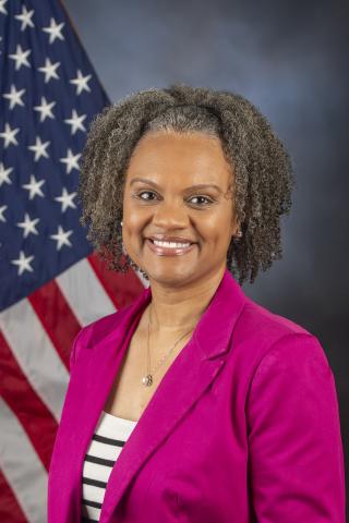 Renee Coker wearing a pink blazer in front of the U.S. flag.