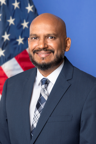 Man in suit and tie smiling in front of American flag.