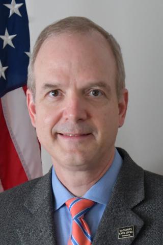 Man in business suit smiling with American and military flags.