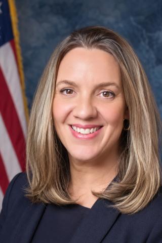 Smiling woman in suit with American flag in background.