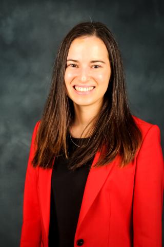 Woman in red blazer and black shirt smiling against a gray background.