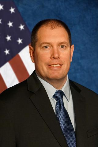 Man in suit and tie smiling in front of American flag.