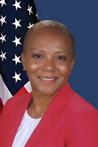 Smiling woman in red blazer in front of American flag.