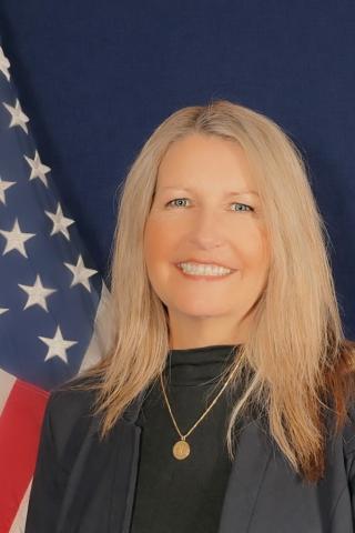 Blonde woman smiling in front of American flag.