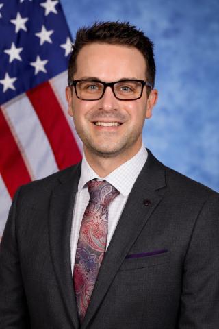 Man in suit and tie standing in front of American flag.
